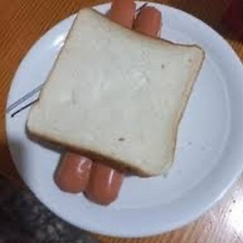 Five Guys - A single slice of plain white bread is placed on top of two hot dogs, which are on a white ceramic plate. The plate rests on a wooden surface, and the hot dogs are partially visible beneath the bread. The image appears to be taken indoors, possibly in a casual dining or home setting. - Burgers Near Me - Middleton, Wisconsin