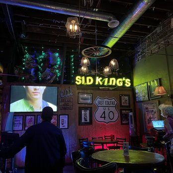 The Owl Saloon - a man standing in front of a large screen - Bars Near Me - Denver, Colorado