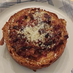 Egg and Cheese Quiche - A baked pastry with a golden-brown, flaky crust, topped with melted cheese, small pieces of bacon or ham, and herbs. The pastry is presented on a white plate with a blue pattern, and the image captures the detailed texture of the toppings and crust.