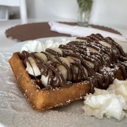 Nelikona Cafe - A waffle with whip cream, banana, Nutella, and powdered sugar on top