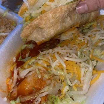 Paco's - A taco with shredded cheese, lettuce, and a crispy shell is held by a person's hand, with additional toppings visible. - Mexican Near Me - Tucson, Arizona