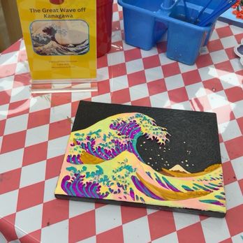 Crafty Tomato - A small canvas featuring 'The Great Wave off Kanagawa' is placed on a red and white checkered table, with paintbrushes and containers nearby. - Paint & Sip Near Me - Tempe, Arizona