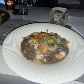 Ara - Short Rib Gnocci was Bomb - A white plate holds short rib gnocchi topped with vegetables and herbs, set on a dining table with a drink and menu nearby. - Mediterranean Near Me - Jupiter, Florida