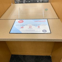 Two lines but no one has even said hello to me - The image shows a CVS Pharmacy checkout counter with a digital screen displaying information about CarePass membership benefits, including exclusive offers and savings. The counter has a wooden finish with clear acrylic dividers, and in the background, shelves are stocked with various packages and products. The setting appears to be inside a retail store, with a focus on the checkout area and promotional signage.