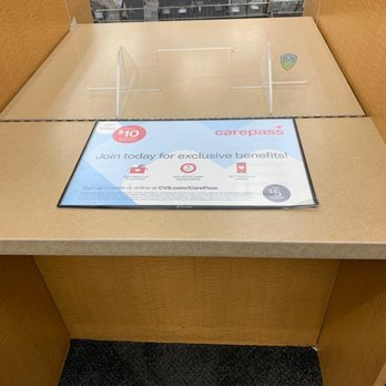 CVS Pharmacy - Two lines but no one has even said hello to me - The image shows a CVS Pharmacy checkout counter with a digital screen displaying information about CarePass membership benefits, including exclusive offers and savings. The counter has a wooden finish with clear acrylic dividers, and in the background, shelves are stocked with various packages and products. The setting appears to be inside a retail store, with a focus on the checkout area and promotional signage. - Drugstores Near Me - Phoenix, Arizona