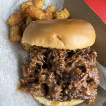 5 Thumbs BBQ - Brisket sandwich with tots - A pulled pork sandwich with barbecue sauce on a bun, accompanied by fried tater tots in a paper tray. - Barbeque Near Me - Indianapolis, Indiana