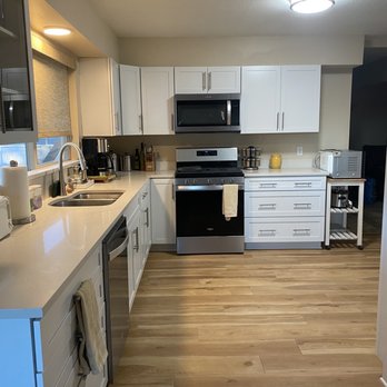Strahle Tile & Granite - Kitchen remodel w Quartz top. - A kitchen featuring white cabinetry, stainless steel stove and microwave, and wooden flooring. Countertops hold small appliances and utensils. - Flooring Near Me - Albuquerque, New Mexico