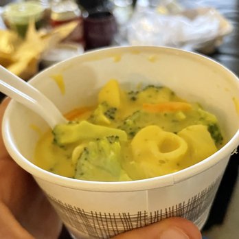 Panera Bread - A paper cup filled with a creamy vegetable soup containing broccoli, carrots, and potatoes, with a plastic spoon inside. - Sandwiches Near Me - Leesburg, Virginia