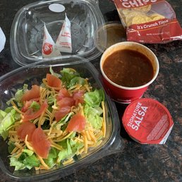 a bowl of salad and a container of chili a bowl of salad and a container of chili