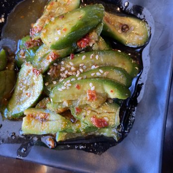 Zu Hot Pot - Cucumber salad with vinegar - A cucumber salad with sliced cucumbers, vinegar, red chili flakes, and sesame seeds served on a black plate. - Hot Pot Near Me - Albuquerque, New Mexico