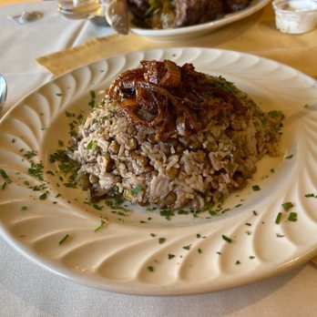 Cedars Restaurant - Ejamel - A serving of rice and lentils garnished with chopped herbs and topped with caramelized onions, presented on a decorative white plate. - Lebanese Near Me - Camp Hill, Pennsylvania