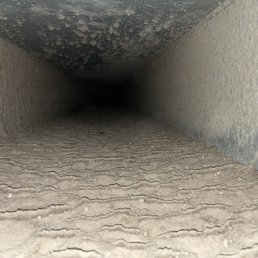 The return duct before cleaning. - A photograph showing the inside of a narrow duct or pipe with a textured, dusty surface and a dark, unknown end.