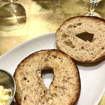Giardino - Toasted Perfectly - Two toasted bagel halves with a hole in the center are placed on a white plate, accompanied by a small dish of butter, on a gold-colored table. - Juice Bars & Smoothies Near Me - Everett, Massachusetts