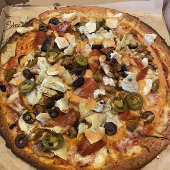 MOD Pizza - A pizza with a slightly charred crust topped with black and green olives, artichoke hearts, pepperoni slices, and melted cheese, served in a cardboard box. The pizza appears freshly baked with a variety of toppings distributed evenly across the surface. - Pizza Near Me - Gainesville, Virginia
