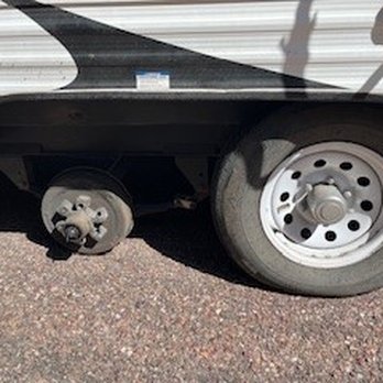 Laforge Towing - The image shows the rear wheel of a vehicle, likely a van or truck, with a flat tire and a missing hubcap. The vehicle is parked on a paved surface, and the wheel's condition indicates it may need repair. The vehicle's body is partially visible, with a shadow cast on the ground. - Towing Near Me - Payson, Arizona