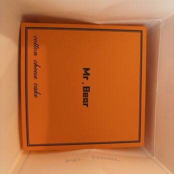Mr Bear - An orange card with black text reading "Mr. Bear" and "cotton cheese cake" is placed inside a box, likely from a bakery. - Desserts Near Me - Queens, New York