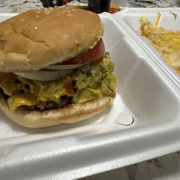 1/2 lb GCCB was delicious - A cheeseburger with lettuce, tomato, onion, and mustard in a bun, served on a foam tray with a side of cheesy enchilada.