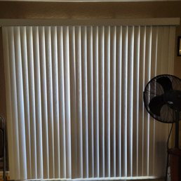 Vertical blinds made of fabric or vinyl cover a large window or sliding door, with light filtering through the slats.