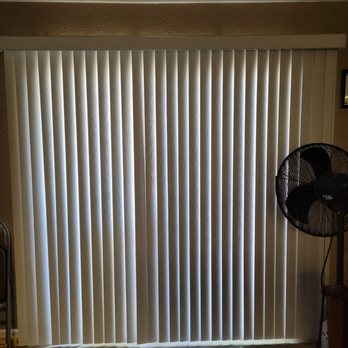 Sun Blinds - Vertical blinds made of fabric or vinyl cover a large window or sliding door, with light filtering through the slats. - Shades & Blinds Near Me - Baldwin Park, California