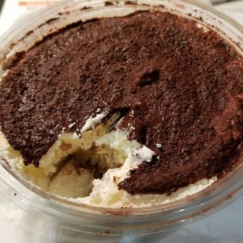 Pizzeria Bruno - Glorious, smooth, custardy, homemade Tiramisu for dessert - A plastic container holds a tiramisu dessert with a layer of cocoa powder on top and a portion taken out, revealing the creamy interior. - Italian Near Me - Sutton, Massachusetts