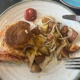 Breakfast croissant with ham, bacon, egg, tomato and cheese with breakfast potatoes & sautéed onions