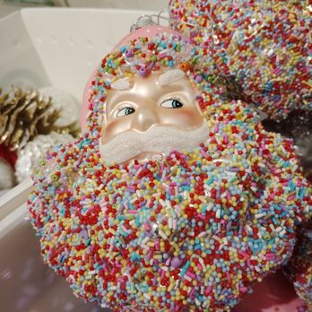 Dillard's - Unusually sweet looking Xmas ornament! - A decorative Christmas ornament with a Santa face, surrounded by a hat covered in multicolored sprinkles, displayed on a store shelf. - Department Stores Near Me - Reno, Nevada
