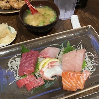 Mikuni - Sashimi platter - A metal tray holds an assortment of sashimi including tuna, salmon, and other fish, garnished with shredded daikon and green leaves. The table also features miso soup, a glass of water with lemon, and other dishes. - Japanese Near Me - Davis, California
