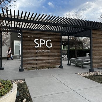 Sports Page Grill - a woman sitting on a bench under a pergol - American Near Me - Dallas, Texas Sports Page Grill - a woman sitting on a bench under a pergol - American Near Me - Dallas, Texas