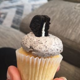 a person holding a cupcake with ore cookies on top a person holding a cupcake with ore cookies on top