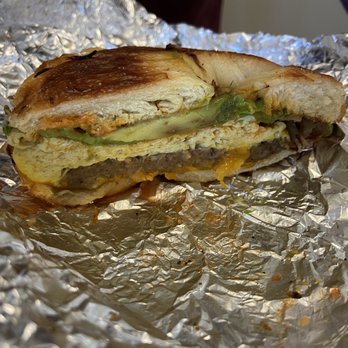Common Ground - Meat, Egg and Cheese sandwich - A partially eaten breakfast sandwich featuring egg, cheese, and beef on toasted bread, resting on crinkled aluminum foil. - Coffee & Tea Near Me - Baltimore, Maryland