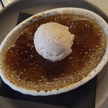 The Standard - Strawberry Crème Brûlée - A crème brûlée dessert topped with a scoop of vanilla ice cream, served in a white oval dish on a tray with a black napkin. - Desserts Near Me - Hamilton, Ontario