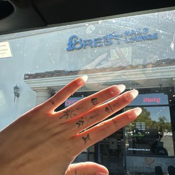Forest Nails Lounge - the ugliest chrome short chunky nails i've ever seen. a 5 year old could do better. - A hand with multiple tattoos on fingers is held up in front of a car window, showing a storefront sign that reads 'Forest Nails Lounge' in the background. - Nail Salons Near Me - Temecula, California