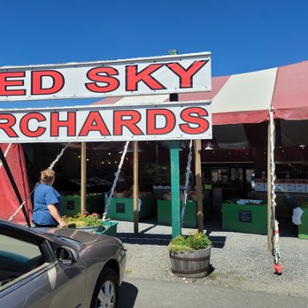 Red Sky Orchards - a woman standing in front of a red sky orchards sign - Fruits & Veggies Near Me - Cle Elum, Washington Red Sky Orchards - a woman standing in front of a red sky orchards sign - Fruits & Veggies Near Me - Cle Elum, Washington