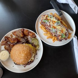 Chicken Parm - A burger with bacon, pickles, and a side of sauce, alongside a pasta dish topped with chicken Parmesan and cheese.