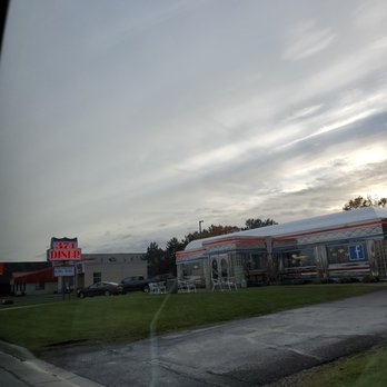 371 Diner - Coming into to restaurant - Exterior of 371 Diner with a lit sign, parking lot, and a building with a Facebook logo, under a cloudy sky. - American Near Me - Baxter, Minnesota
