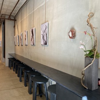 Sushi Muse - a long table with stools and pictures on the wall - Sushi Bars Near Me - New York, New York