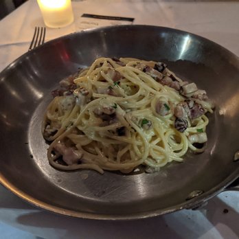 Assaggio - A serving of pasta with a creamy sauce, pieces of meat, and herbs is presented in a metal pan on a dining table with a candle and utensils. - Italian Near Me - Boston, Massachusetts