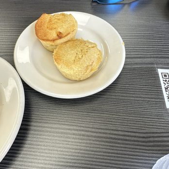 Cajun Breakfast Joint - Two golden-brown biscuits are placed on a white plate on a dark, textured table. Blue sunglasses are positioned nearby, reflecting the surroundings. - Breakfast & Brunch Near Me - Phoenix, Arizona