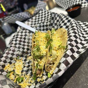 Effingbar And Grill - Taco Tuesday - A taco filled with shredded cheese, chopped lettuce, and ground beef is presented on black-and-white checkered paper in a casual dining environment. The taco shell appears crispy, and the toppings are fresh. In the background, there are other food items, drinks, and restaurant patrons, indicating a lively atmosphere. The image captures a typical taco Tuesday meal at a casual eatery. - American Near Me - Albuquerque, New Mexico