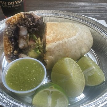 Dulce Cielo MX - A burrito served in a foil container with lime wedges, green sauce, and a drink from Cold Dhaka Coffee House on a dark wooden table. - Mexican Near Me - Beacon, New York