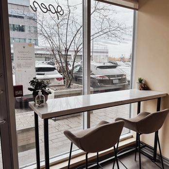 Tangy Cafe - Two white chairs are positioned at a high table near a large window in a cafe, with parking and trees visible outside. - Cafes Near Me - Markham, Ontario