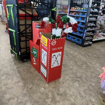 Dollar Tree - Christmas decorative trees are displayed in a red box labeled 'Tinsel Decor' in a store aisle with hardware and battery supplies. - Discount Store Near Me - Springfield, Virginia