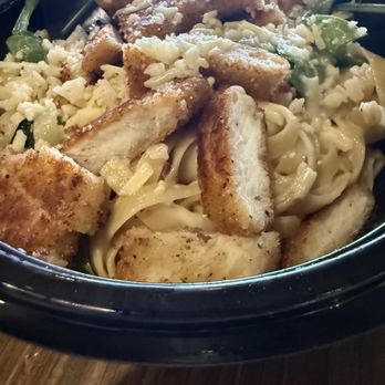 Noodles and Company - A bowl of chicken Caesar salad containing grilled chicken pieces, croutons, shredded cheese, and chopped greens, served in a black bowl. - Noodles Near Me - Tempe, Arizona