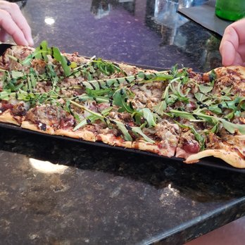Table One - a person cutting a pizza on a cutting board - New American Near Me - Fond du Lac, Wisconsin Table One - a person cutting a pizza on a cutting board - New American Near Me - Fond du Lac, Wisconsin