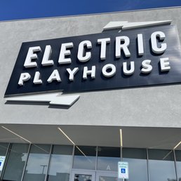 Front entrance sign - Exterior sign for Electric Playhouse, an entertainment venue, mounted on a gray building facade with reserved parking signs below.