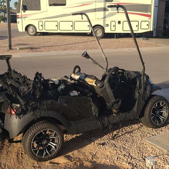 Action Golf Carts - A severely burned golf cart is situated on a sandy patch next to a paved sidewalk, with a recreational vehicle and a building in the background. - Golf Cart Rentals Near Me - Mesa, Arizona