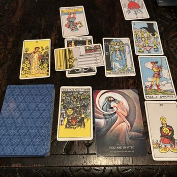Oothoon's - Multiple tarot cards are spread out on a dark wooden table, including The High Priestess, King of Pentacles, and Page of Swords, with a 'You Are Invited' card in the center. - Spiritual Shop Near Me - Memphis, Tennessee