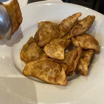 Jibek Jolu - Fried pierogi/vareniki $15 - The image features a white plate with several fried pierogi or vareniki, a traditional Central Asian dish, arranged on it. The pierogi are golden-brown and appear crispy. The background shows a restaurant interior with dark furniture and a casual dining atmosphere. The dish is being served, possibly with a side or dipping sauce, and the setting suggests a relaxed dining experience. - Russian Near Me - Glenview, Illinois
