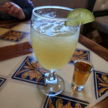 Fiesta  Acapulco - House margarita. Separate order of Grand Marnier. - A glass of house margarita with a lime wedge is placed on a decorative tile table at a restaurant, with a small shot of tequila nearby. - Mexican Near Me - Newburgh, Indiana