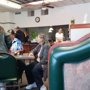 Vasili's Corner Cafe - people sitting at tables - A group of people are seated at tables in a casual restaurant, with some standing and serving. The interior features simple decor and a visible kitchen area. - Cafes Near Me - Elkhorn, Wisconsin